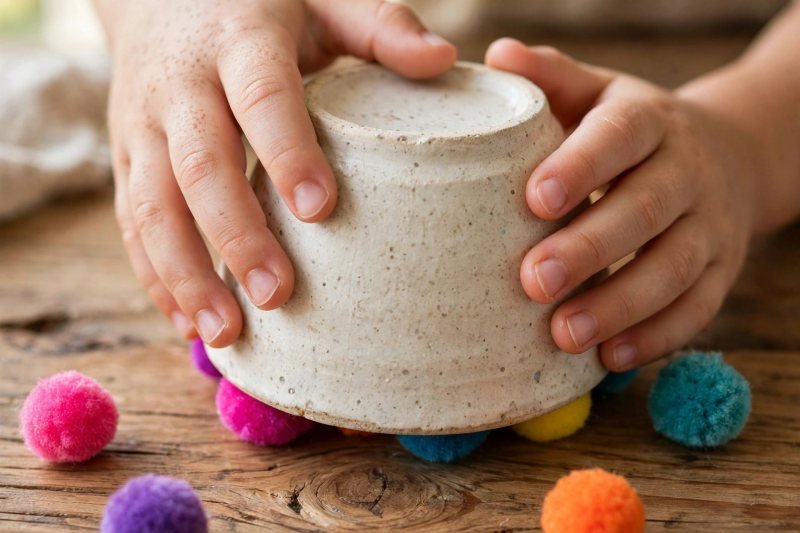 Small hands hiding pom-pom counters under an upside-down cup on a table